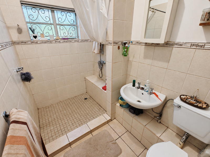 A functional bathroom featuring a walk-in shower, pedestal basin, and toilet, finished with neutral wall and floor tiling.