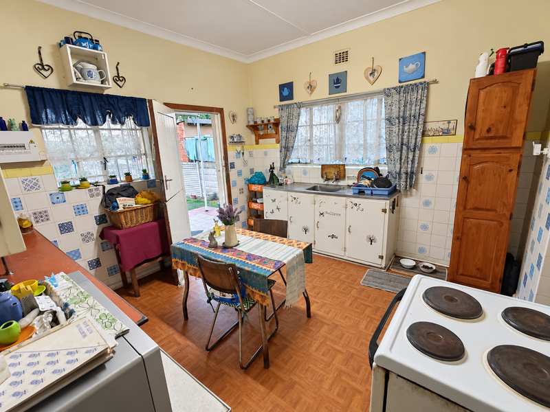 A dated kitchen featuring original cabinetry, tiled splashbacks, and a functional layout with direct access to the rear exterior.