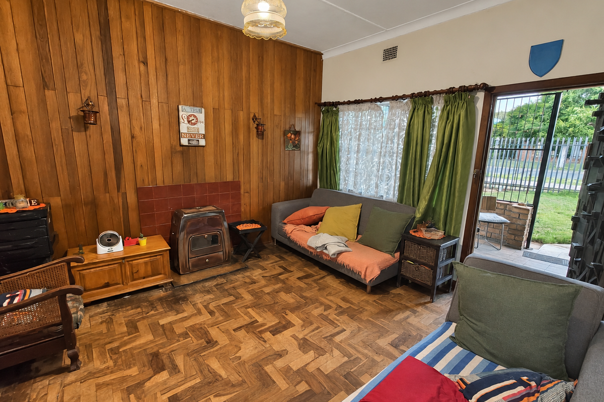 A living room featuring classic parquet flooring, wood-paneled walls, and a freestanding fireplace, with direct access to the outdoor area through a sliding door.