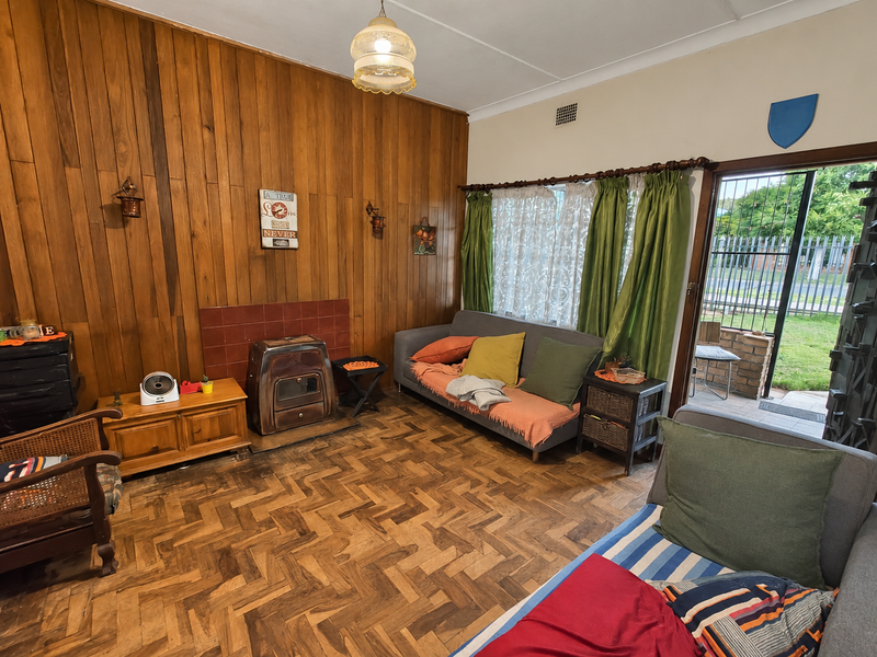 A living room featuring classic parquet flooring, wood-paneled walls, and a freestanding fireplace, with direct access to the outdoor area through a sliding door.