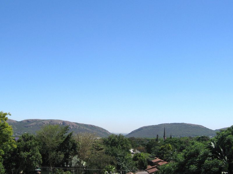 A scenic elevated view overlooking lush green trees and distant hills under a clear blue sky.