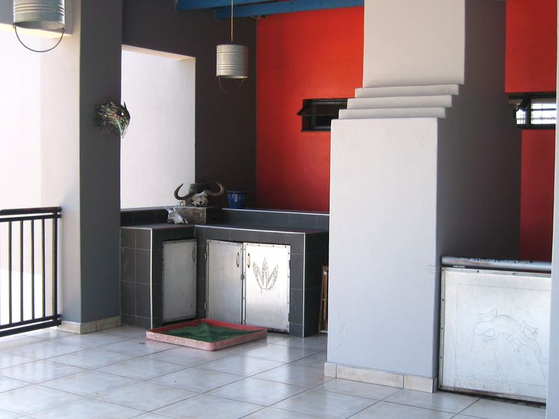 Covered patio area featuring a built-in braai, tiled flooring, and metal cabinetry, providing a functional outdoor entertainment space.