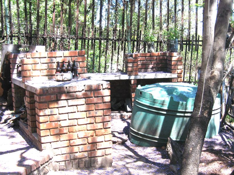 Outdoor entertainment area featuring a rustic brick built-in braai with concrete countertops and a large water storage tank.