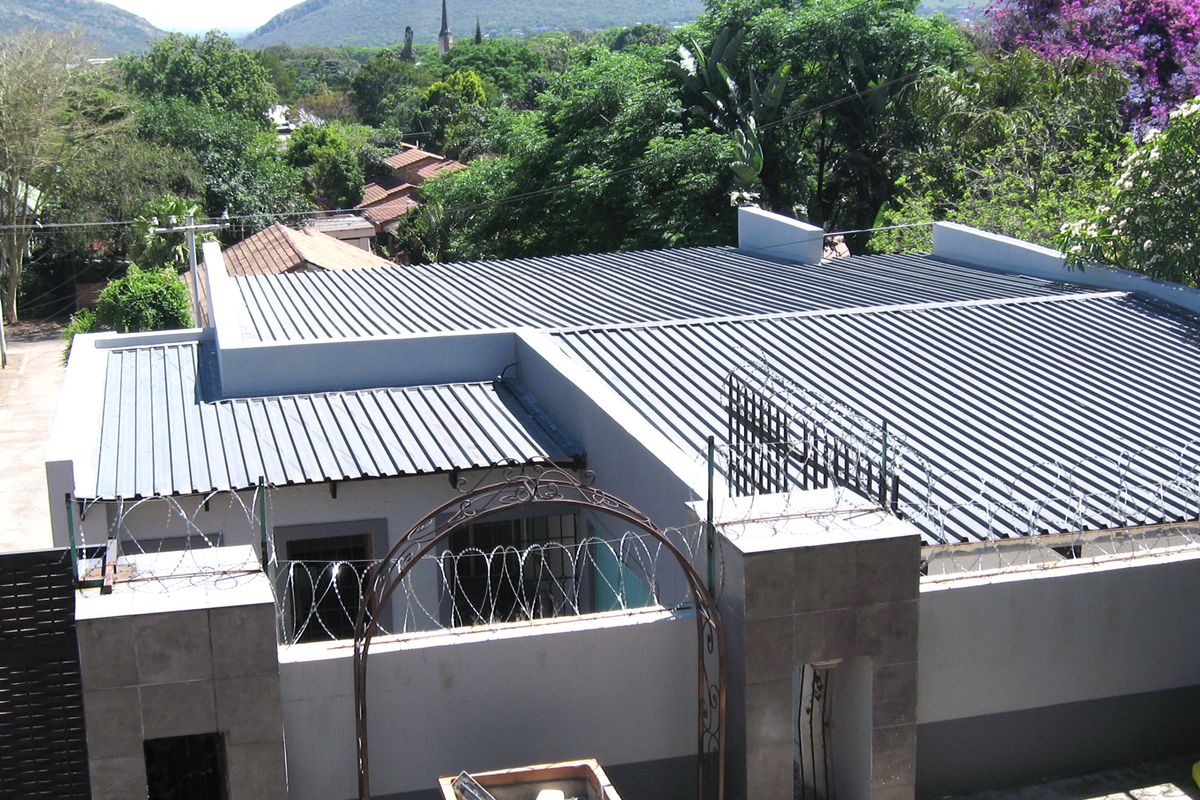 Aerial view of the property showing the corrugated metal roof, perimeter wall with security razor wire, and a decorative metal entrance archway.