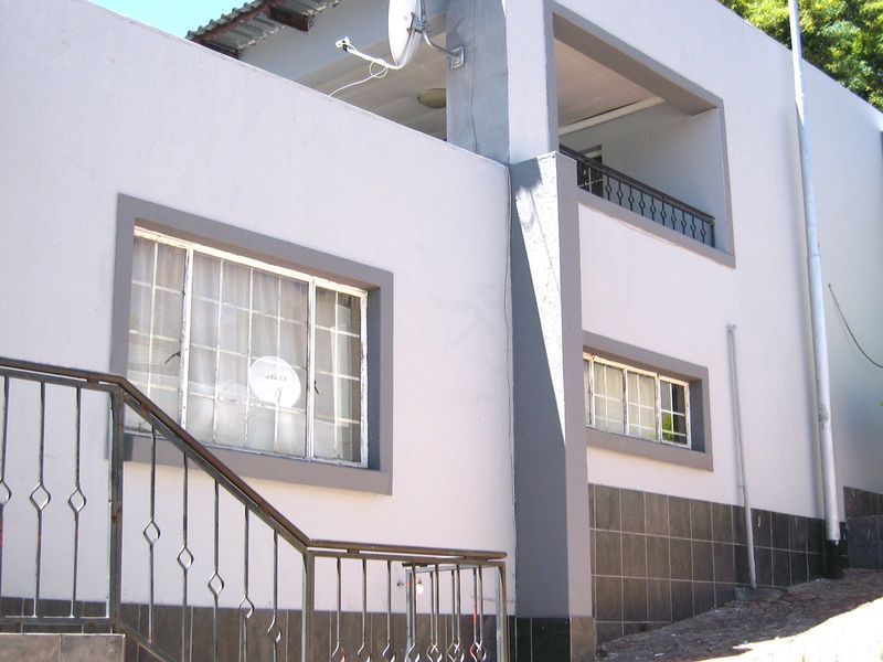 Front elevation of a two-story house featuring a metal balustrade, tiled lower wall finish, and an upper-level balcony.