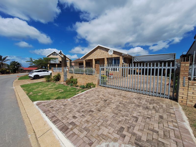 Front view of a brick house featuring a paved driveway, secure metal fencing, and a covered carport area.