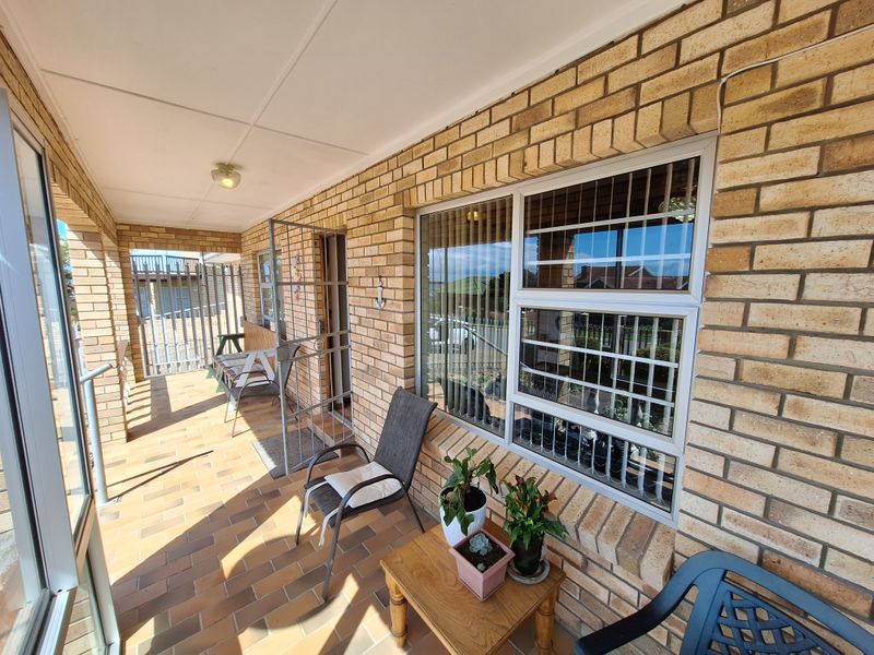 A covered patio area featuring face brick walls, tiled flooring, and secure window bars, providing a functional outdoor space.