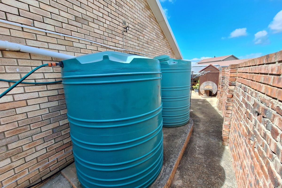 Side exterior area featuring two large water storage tanks positioned along the brick house facade and a concrete pathway.