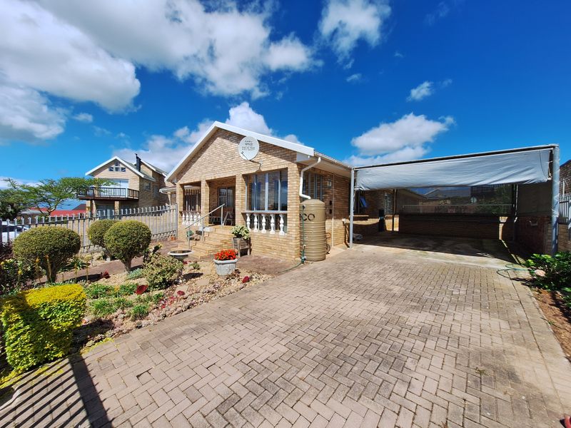 A well-maintained brick house featuring a paved driveway, a covered carport, and a front garden with established landscaping and a water tank.