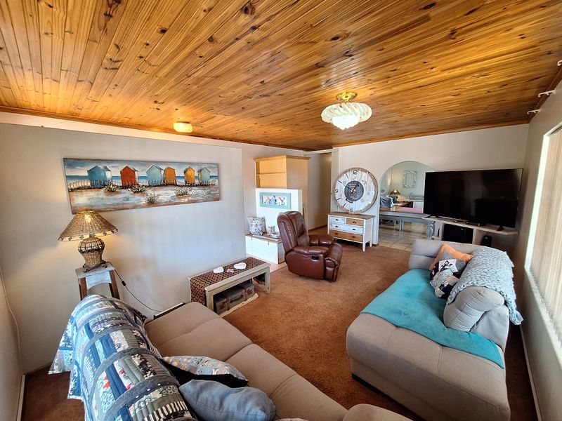 A living room featuring a distinctive timber tongue and groove ceiling, carpeted flooring, and an arched entryway leading to an adjacent space.