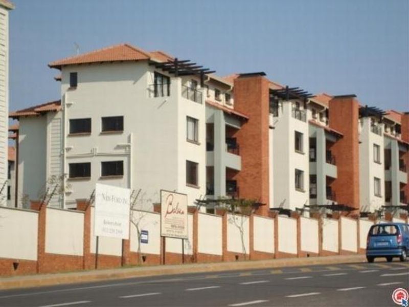 Street view of a multi-story apartment complex featuring brick and plaster facade, tiled roofs, and secure perimeter walling with electric fencing.