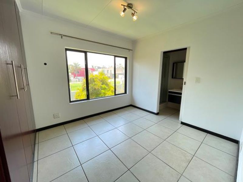 A bright, empty bedroom featuring tiled flooring, built-in cupboards, and an en-suite bathroom access.