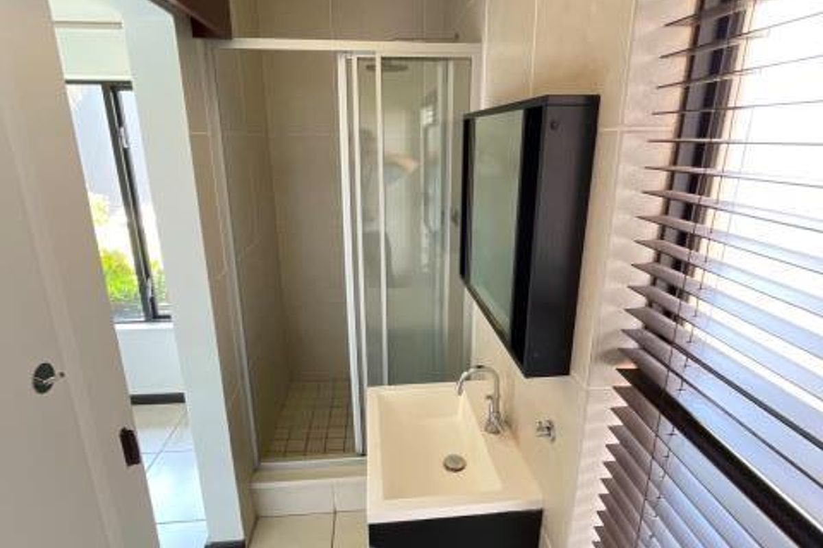 A clean, modern bathroom featuring a shower enclosure, wall-mounted vanity with basin, and tiled finishes throughout.