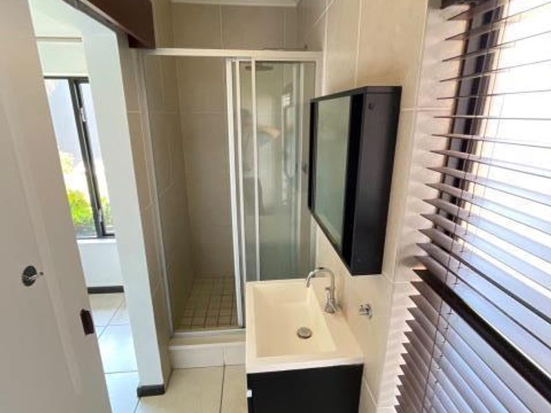 A clean, modern bathroom featuring a shower enclosure, wall-mounted vanity with basin, and tiled finishes throughout.