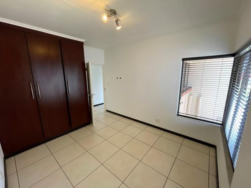 A bright, empty bedroom featuring tiled flooring, built-in wooden cupboards, and venetian blinds on the windows.