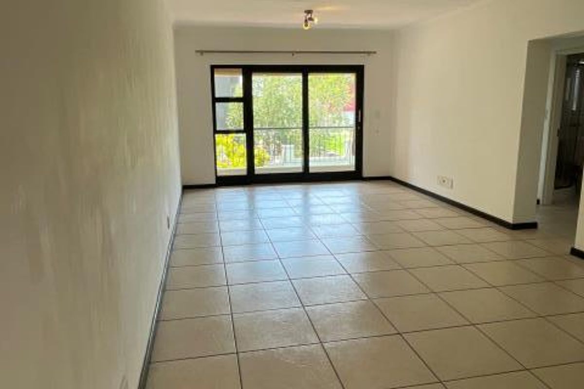 A spacious, empty living area featuring neutral tiled flooring, ceiling-mounted lighting, and a large sliding glass door providing access to the exterior.