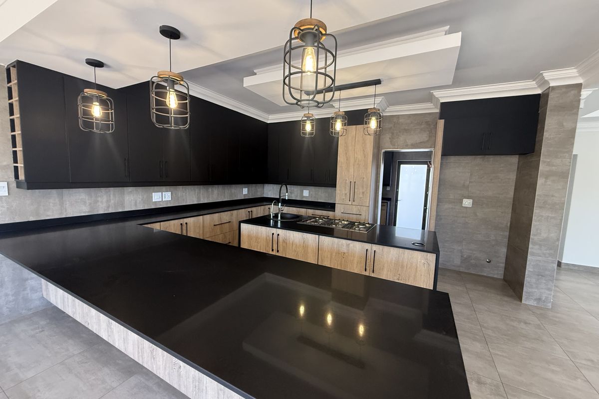 Modern kitchen featuring sleek black stone countertops, contrasting wood-look and matte black cabinetry, built-in gas hob, and stylish industrial-style pendant lighting.
