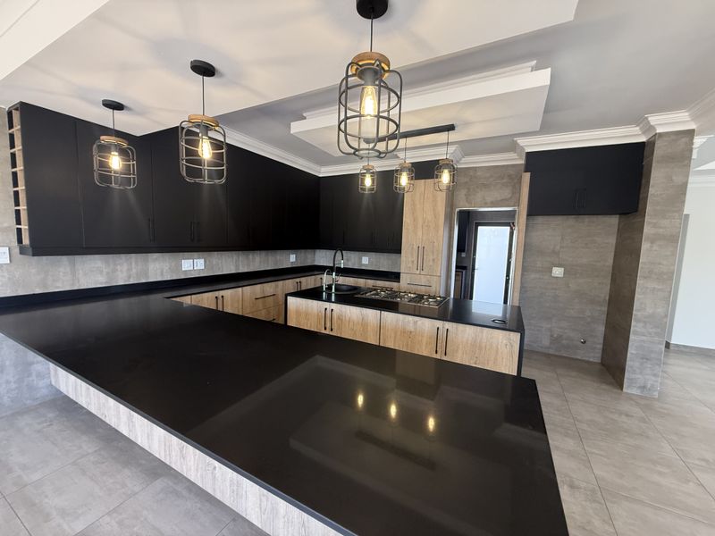 Modern kitchen featuring sleek black stone countertops, contrasting wood-look and matte black cabinetry, built-in gas hob, and stylish industrial-style pendant lighting.