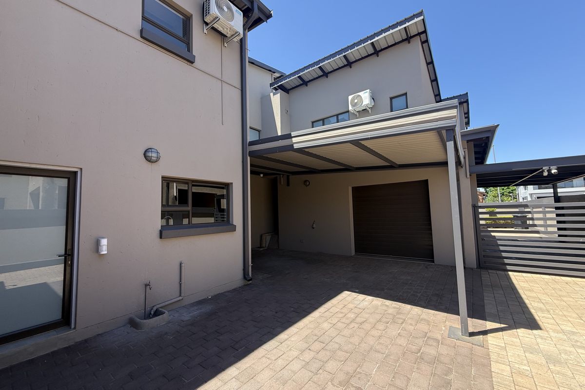 Rear exterior view featuring a paved driveway, covered carport, garage access, and modern exterior finishes with wall-mounted air conditioning units.