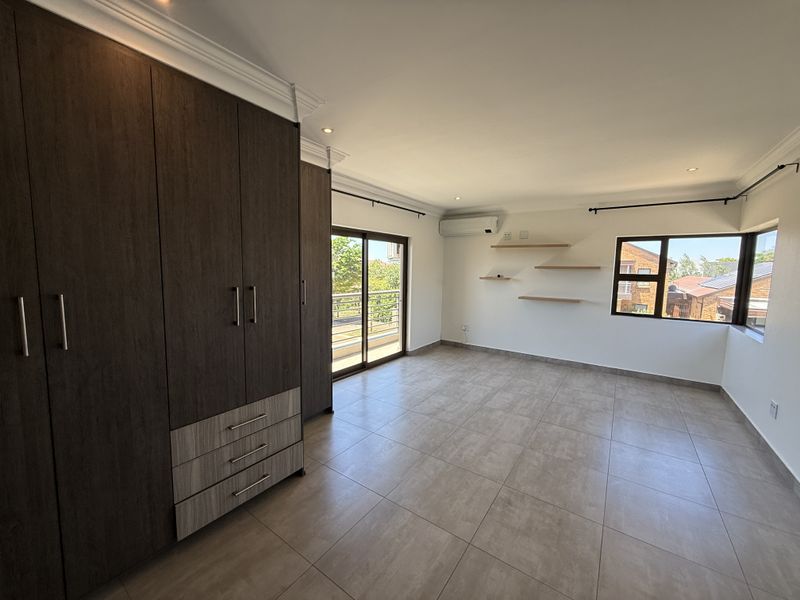 Spacious bedroom featuring modern tiled flooring, extensive built-in cupboards, air conditioning, and a sliding door leading to an outdoor area.