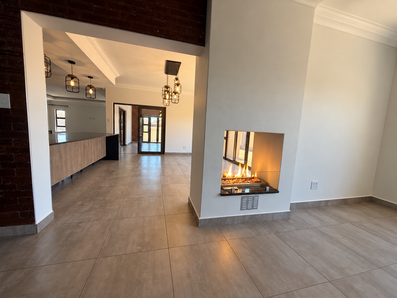 Spacious open-plan living area featuring a modern double-sided fireplace, large format floor tiles, and a contemporary kitchen with island cabinetry.