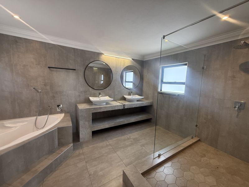 Modern, spacious bathroom featuring a double vanity, built-in bathtub, and a large walk-in shower with glass enclosure, finished with contemporary grey tiling.