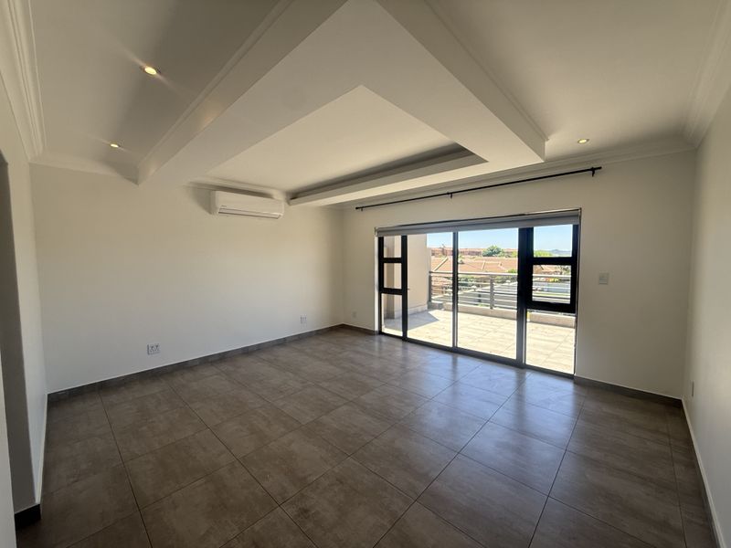 Spacious living area featuring modern tiled floors, a recessed ceiling with downlights, an air conditioning unit, and large sliding doors leading to a balcony.