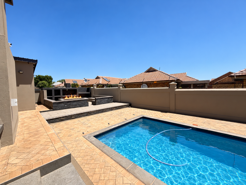 Outdoor entertainment area featuring a swimming pool, paved patio, and a built-in braai with stone cladding, perfect for hosting and relaxation.