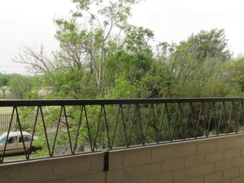 A simple balcony featuring a brick wall and a metal balustrade overlooking a street and green trees.