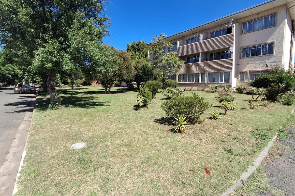 Exterior view of a multi-story townhouse complex featuring a shared garden area, mature trees, and private balconies.