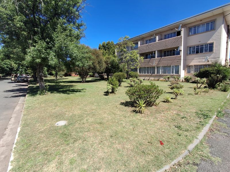 Exterior view of a multi-story townhouse complex featuring a shared garden area, mature trees, and private balconies.