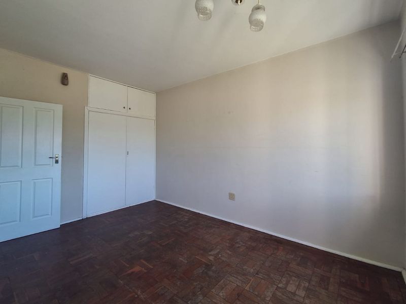 An empty bedroom featuring original parquet flooring and built-in cupboards, offering a blank canvas for renovation or interior design updates.