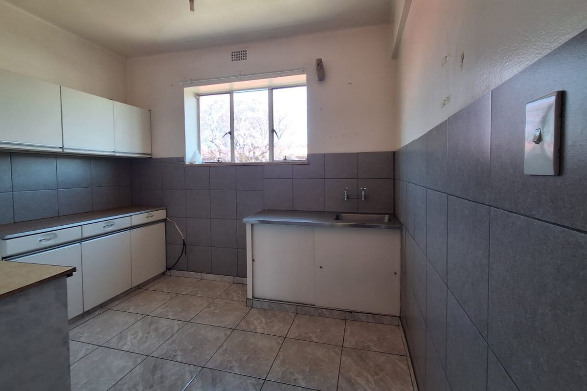 A functional, empty kitchen featuring tiled flooring, grey tiled splashbacks, built-in cabinetry, and a stainless steel sink, ready for a modern update.