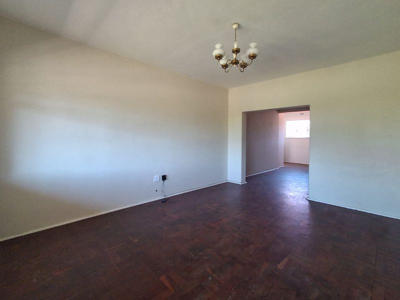 An empty living room featuring original parquet flooring and a central ceiling light fixture, offering a blank canvas for renovation.