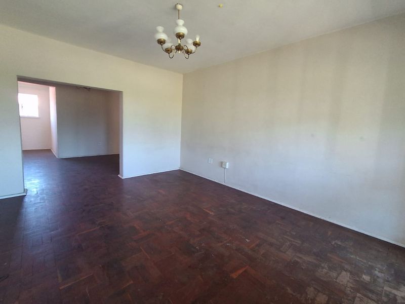 An empty living room featuring original parquet flooring and a central ceiling light fixture, offering a blank canvas for renovation.