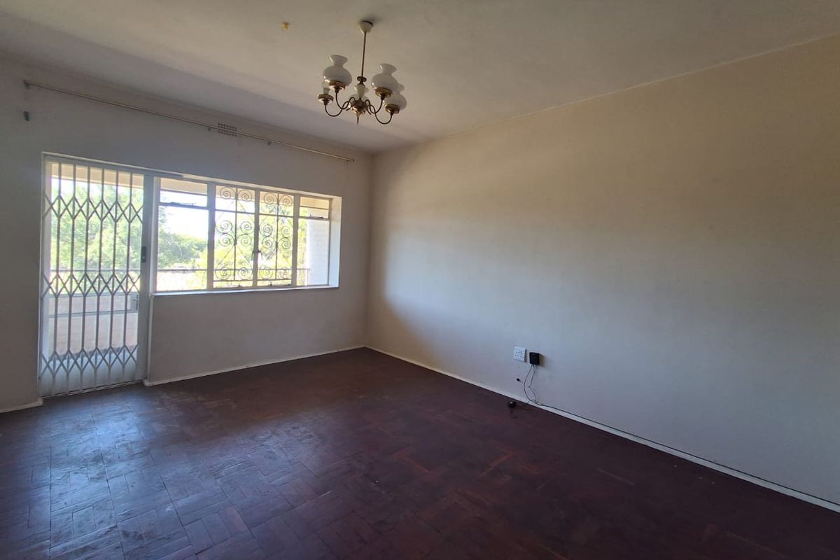 An empty living room featuring original parquet flooring, security gate access, and large windows, offering a blank canvas for renovation and interior design.
