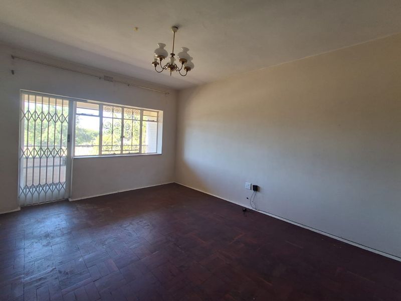 An empty living room featuring original parquet flooring, security gate access, and large windows, offering a blank canvas for renovation and interior design.