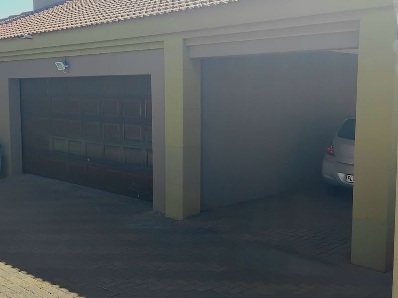 Front elevation of the townhouse featuring a paved driveway, a secure garage door, and a covered carport area.
