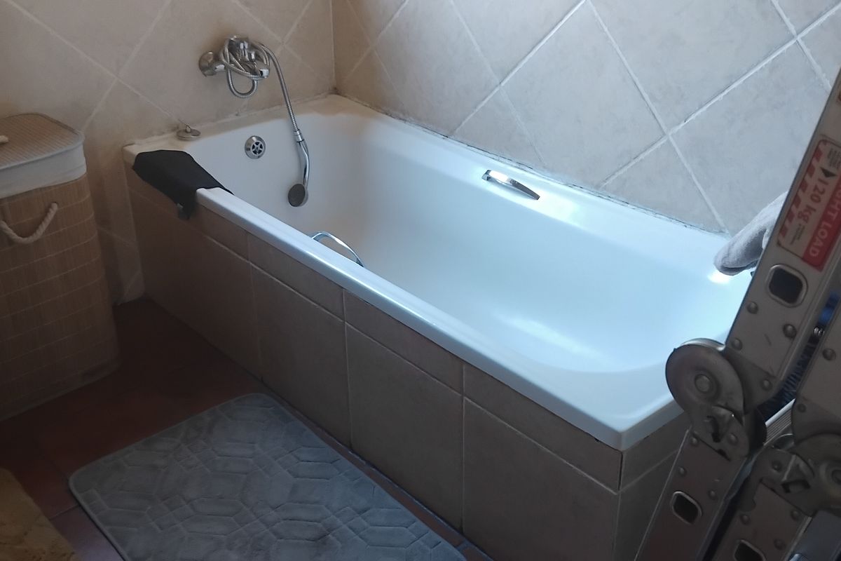 A bathroom featuring a built-in bathtub with wall-mounted mixer tap and tiled surround, showing signs of dated finishes.