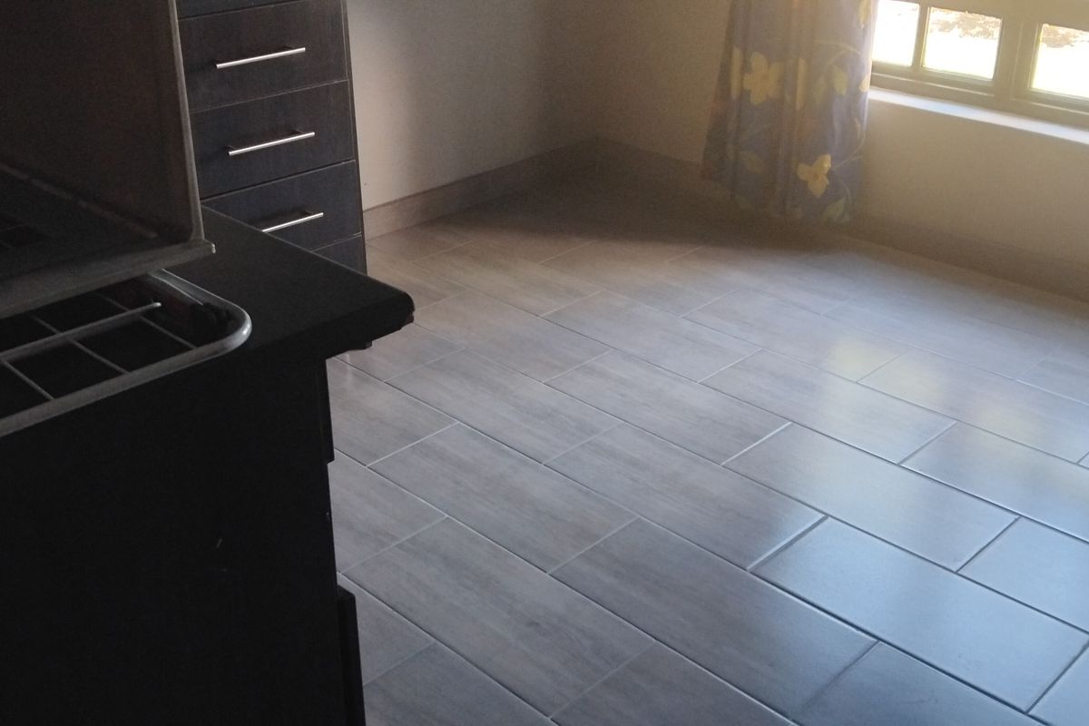 A bright, empty bedroom featuring modern light-toned tiled flooring and a large window, providing a clean and neutral space ready for personalization.