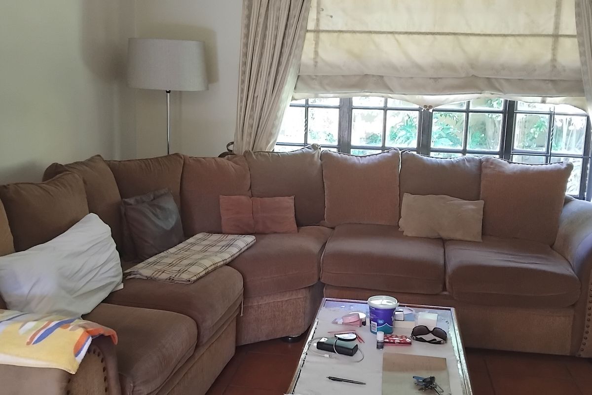 A comfortable living room featuring tiled flooring and a large window with integrated roman blinds and curtain rods.