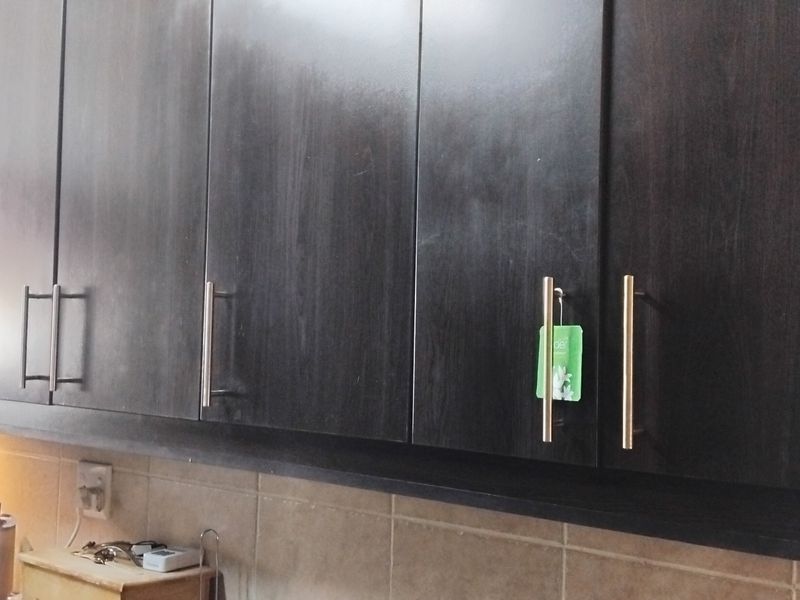 A kitchen area featuring dark wood cabinetry with modern metal handles and a tiled backsplash with integrated under-cabinet lighting.