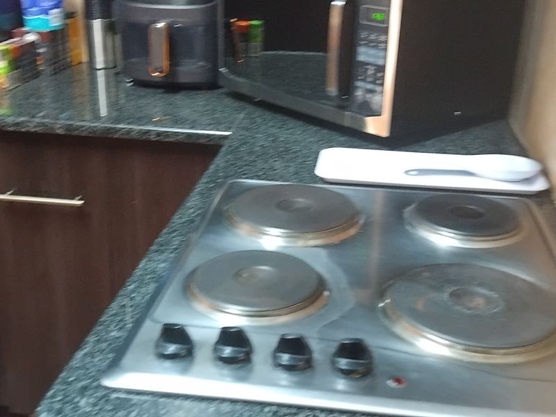 A compact kitchen area featuring dark wood cabinetry, granite countertops, and a four-plate electric hob with a tiled backsplash.