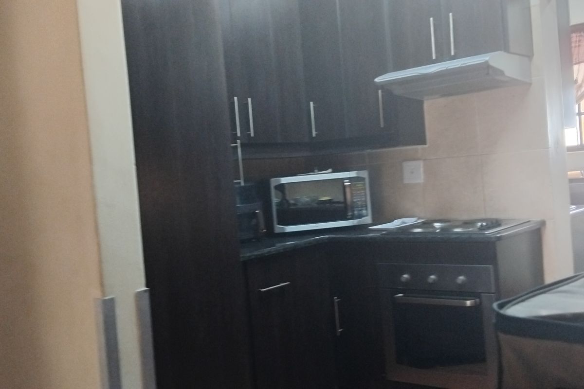 A compact kitchen featuring dark wood cabinetry, built-in oven, electric hob, and extractor fan with a tiled backsplash.