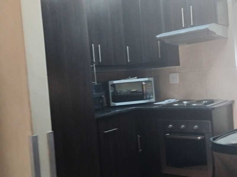 A compact kitchen featuring dark wood cabinetry, built-in oven, electric hob, and extractor fan with a tiled backsplash.