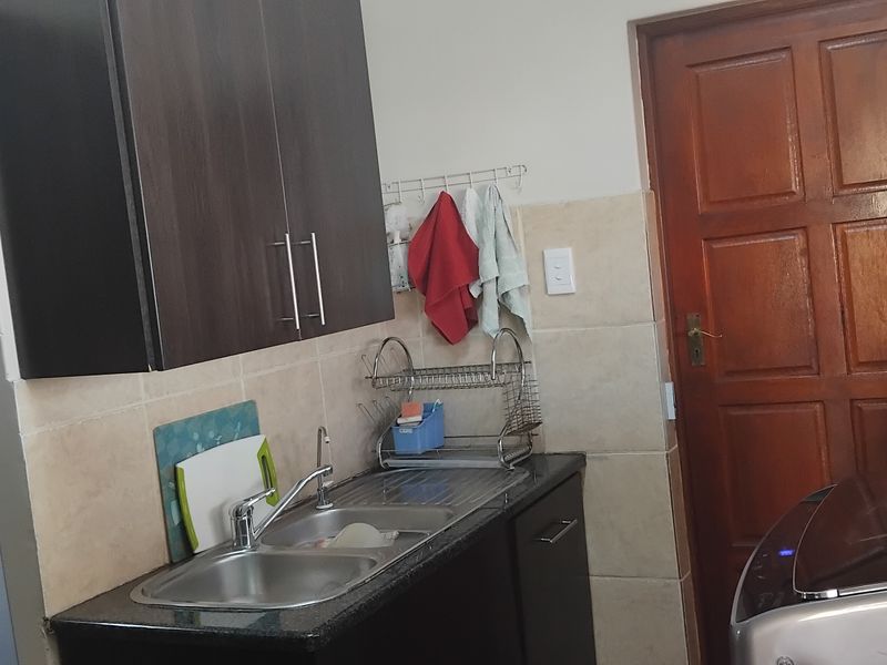 A functional scullery area featuring dark wood cabinetry, granite countertops, a double bowl stainless steel sink, and tiled splashbacks.