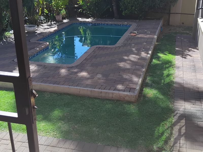 Outdoor pool area featuring a paved deck, surrounding lawn, and direct access from the townhouse.