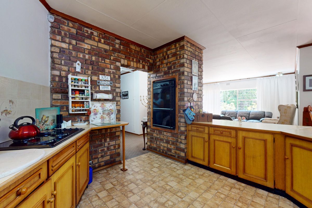 A functional kitchen featuring exposed brick walls, wooden cabinetry, a built-in oven, and a gas hob, with an open-plan layout connecting to the living area.