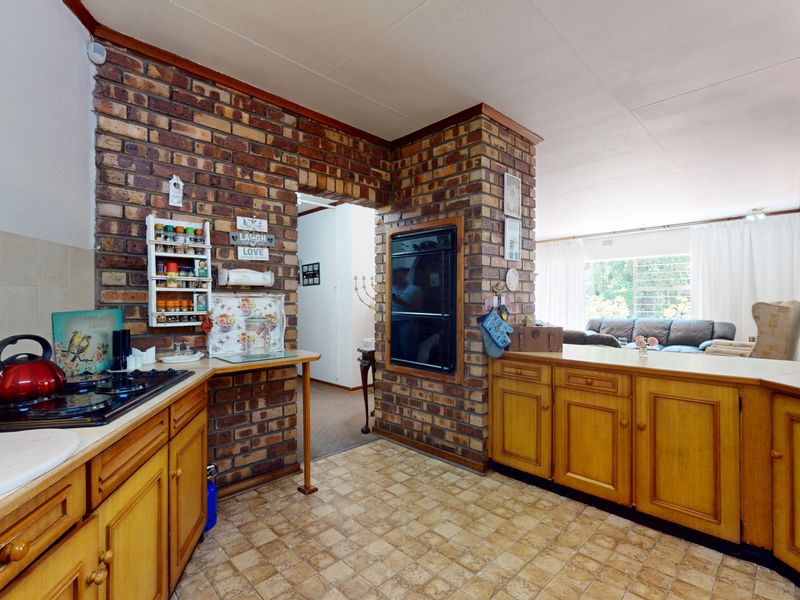 A functional kitchen featuring exposed brick walls, wooden cabinetry, a built-in oven, and a gas hob, with an open-plan layout connecting to the living area.