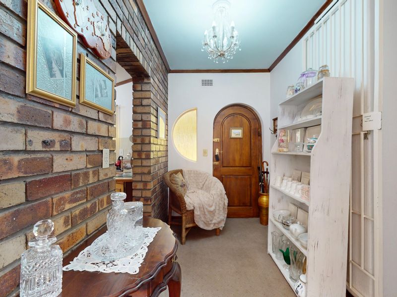 Welcoming entrance hall featuring exposed brickwork, a distinctive arched timber front door, a circular feature window, and a classic chandelier.